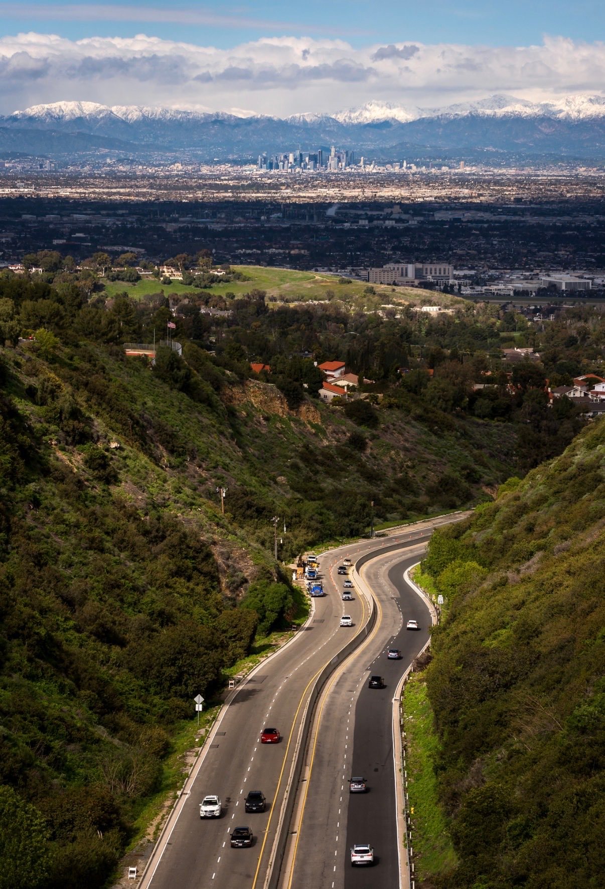 Aerial view of Los Angeles highway with downtown skyline and snow-capped mountains
