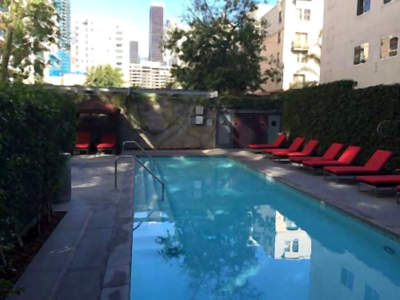 Downtown LA apartment building rooftop pool with red lounge chairs and city skyline views